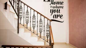 A staircase with ornate metal railings and a wooden handrail, leading to a landing with a wall-mounted sign that reads "Home is where you are." - Host & Home (Valencia)