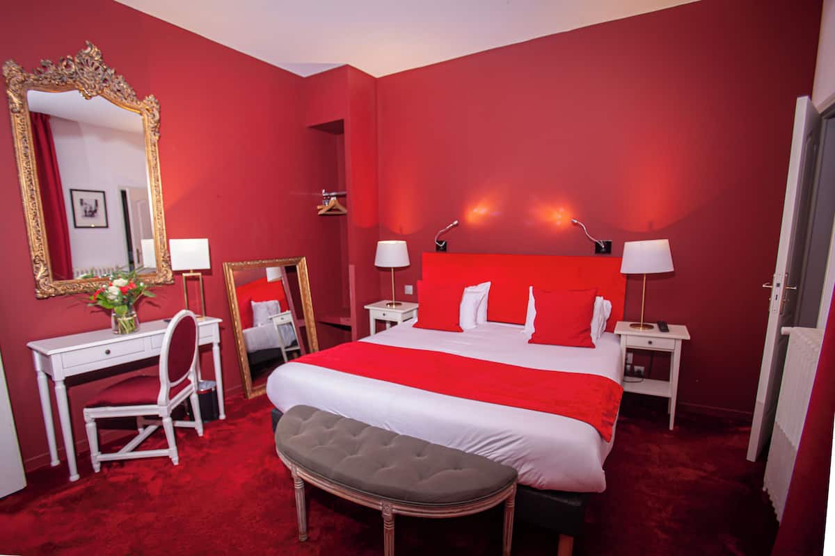 A red-themed hotel room with a large bed, a desk, a chair, and a mirror.