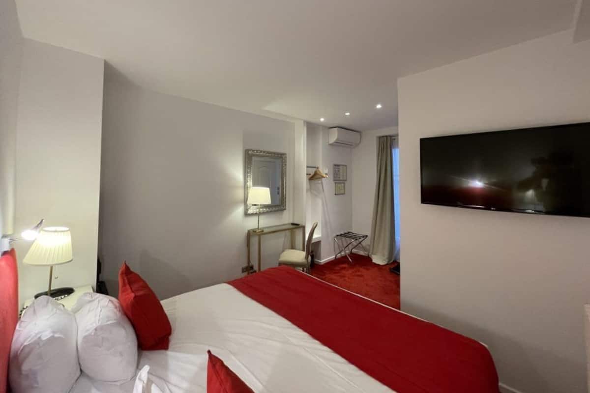 A hotel room with a large bed, a flat-screen TV mounted on the wall, a bedside table with a lamp, and a chair.