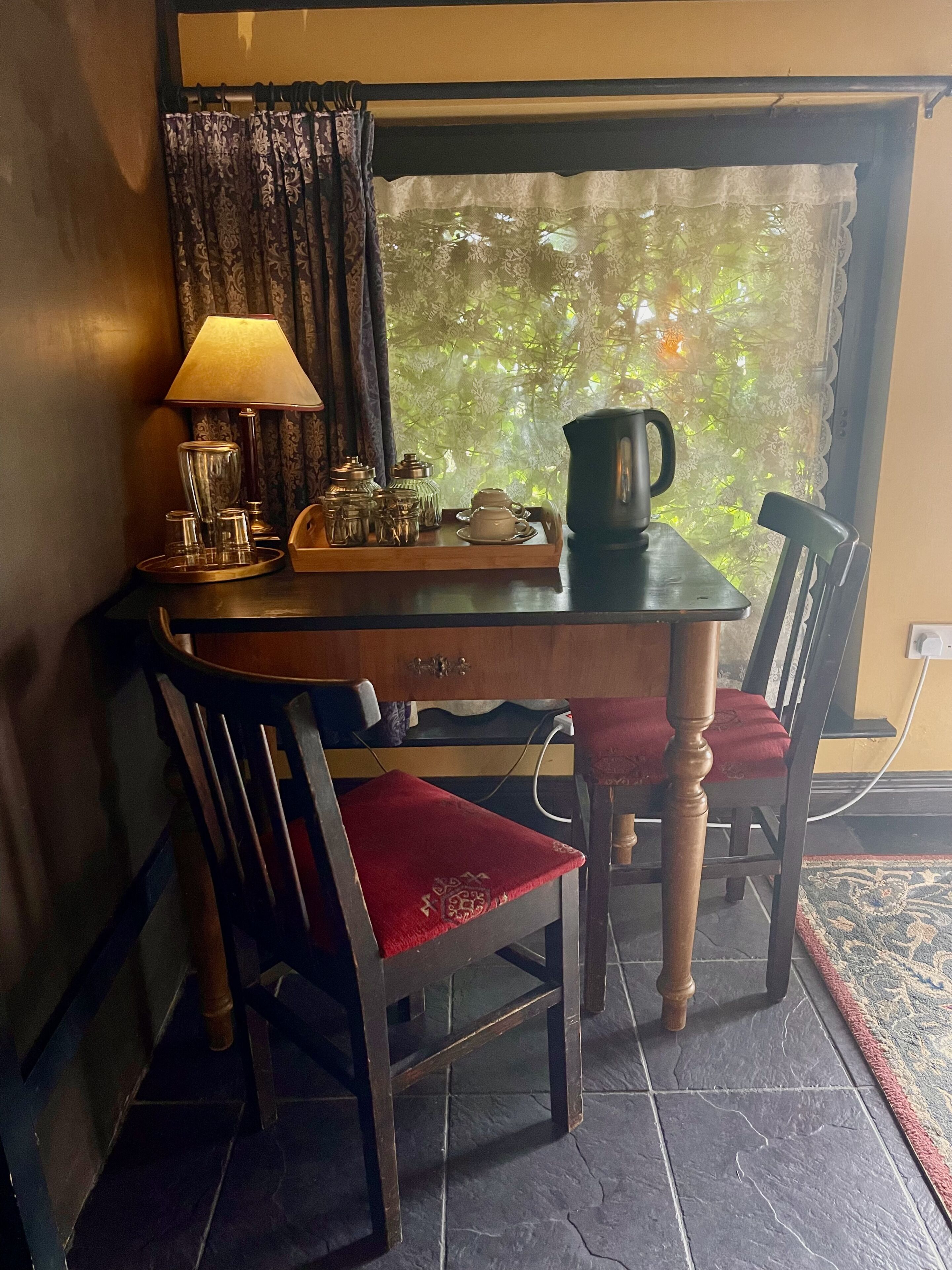 A small dining area with a table set for two, featuring a lamp, teapot, cups, and a tray.