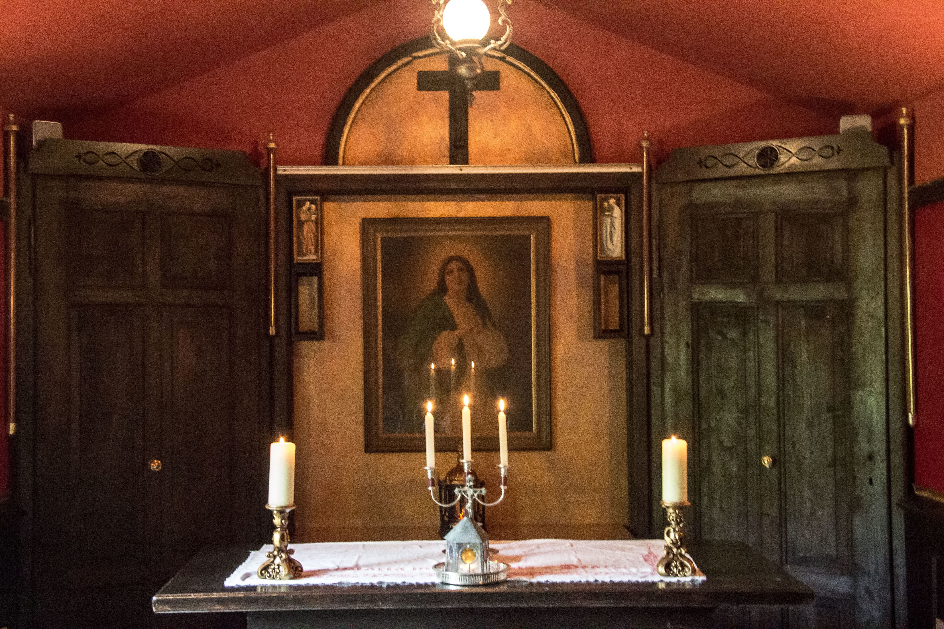 A religious icon with a cross above, a framed painting, and a candelabrum with lit candles on a table.