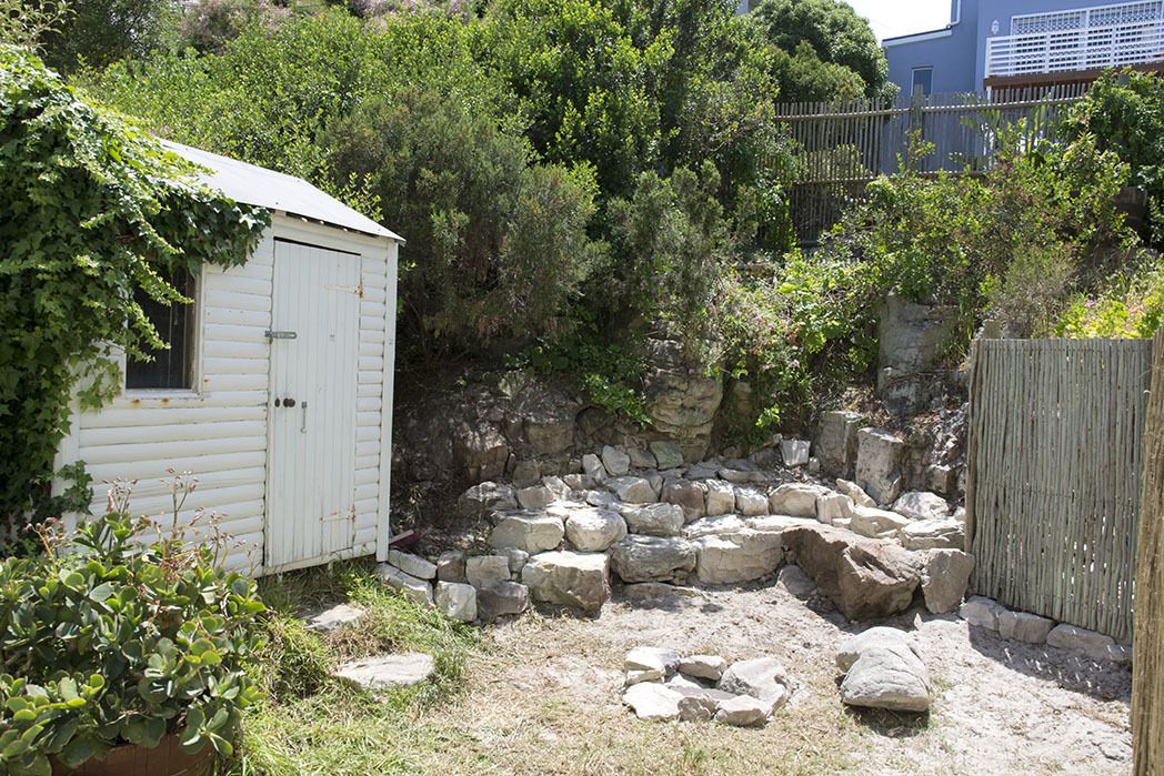 A rustic outdoor area with a wooden shed, a stone wall, and a wooden fence.