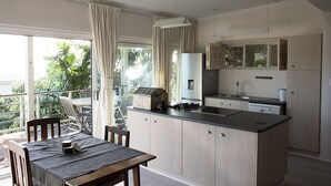Una cocina moderna con una isla central, un comedor con mesa y sillas, y vistas a espacios verdes.