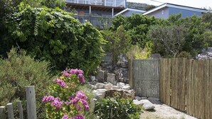 Un jardín con valla de madera, muro de piedra y diversas plantas y flores.
