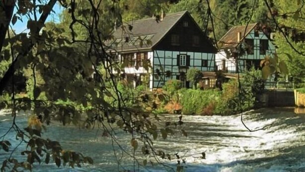 Una casa de estilo tradicional a orillas de un río, rodeada de abundante vegetación y con un río serpenteando.