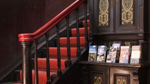 Una escalera con peldaños alfombrados de rojo y barandilla de madera oscura.