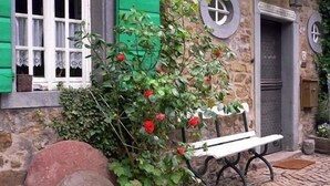 Un edificio de piedra con un banco, una puerta y una ventana con contraventanas verdes.