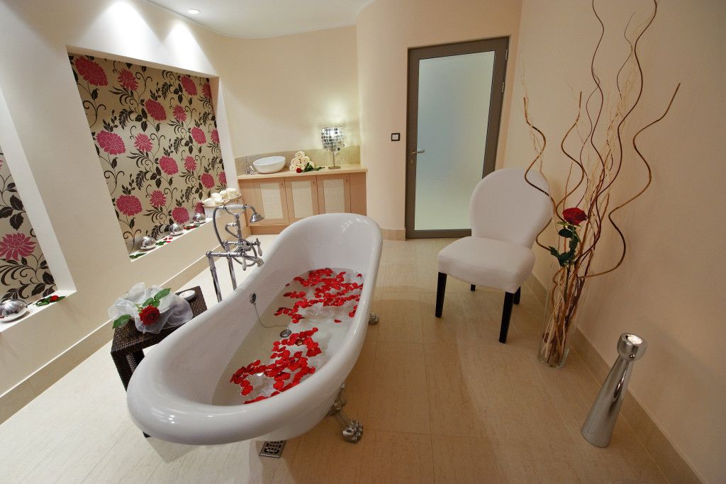 Ein Badezimmer mit freistehender Badewanne, einem weißen Stuhl und einer Vase mit Zweigen.