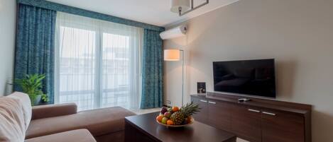 A modern living room with a sofa, a coffee table with a fruit bowl, a TV, and a cabinet.