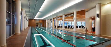 A swimming pool with clear lanes, surrounded by columns and a wooden floor.