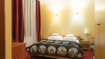 Una habitación de hotel con cama, escritorio, silla, lámpara y armario.