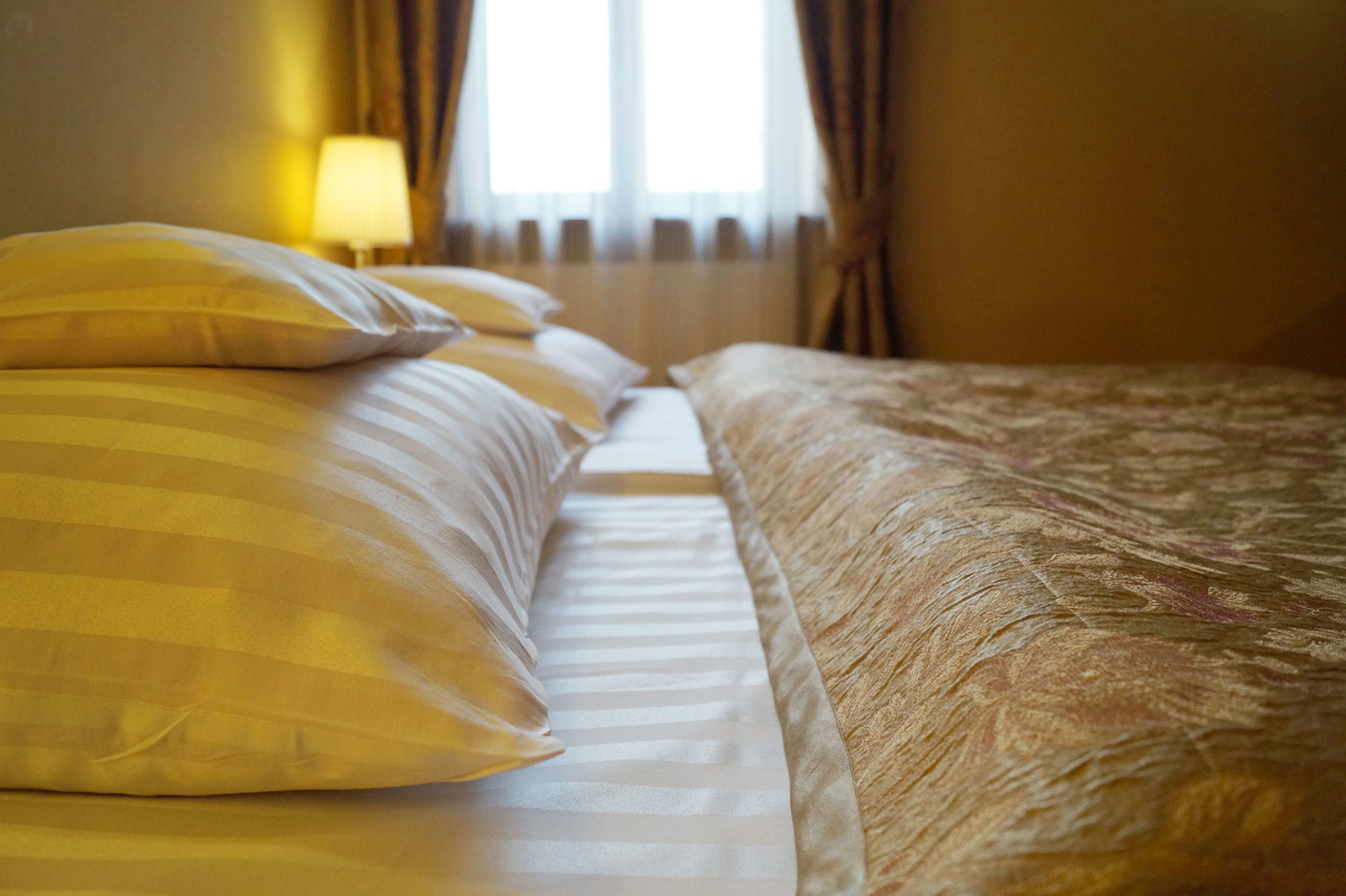 A hotel room with a bed featuring striped and textured bedding, a lamp, and a window with curtains.