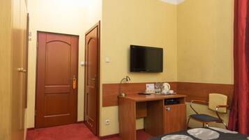 Una habitación de hotel con una cama, un escritorio con televisor, una silla y una puerta.
