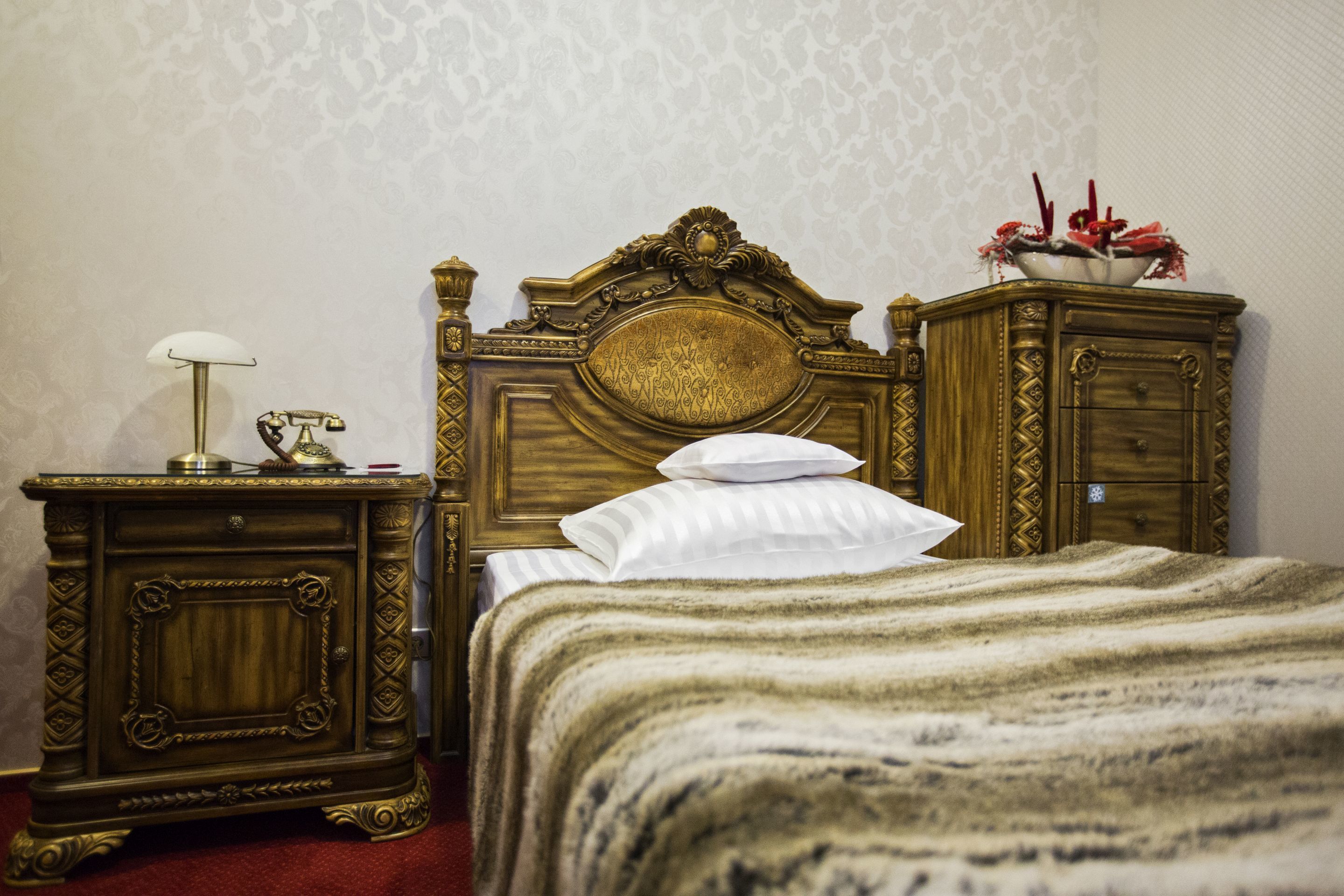 A bedroom with a large bed, a nightstand with a lamp, and a dresser with a decorative bowl on top.