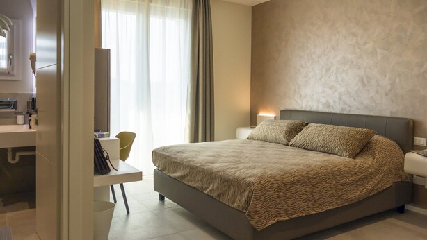 Een moderne slaapkamer met een groot bed, nachtlampjes, een bureau en een stoel.