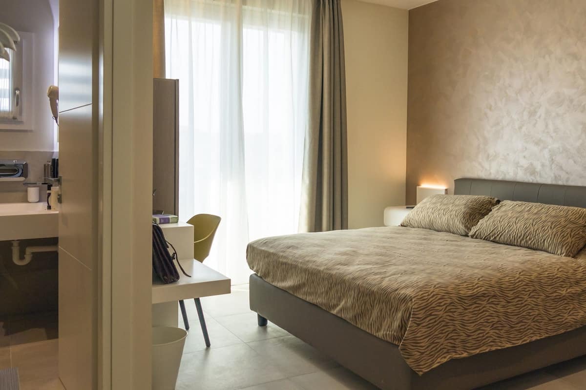 Een moderne slaapkamer met een groot bed, nachtlampjes, een bureau en een stoel.