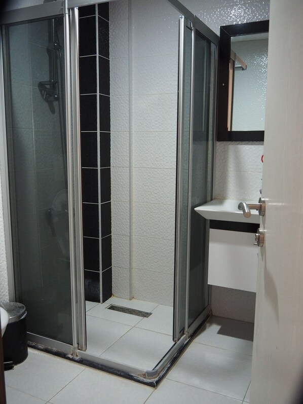 Un baño con ducha de vidrio, un lavamanos blanco y un espejo sobre el lavamanos.