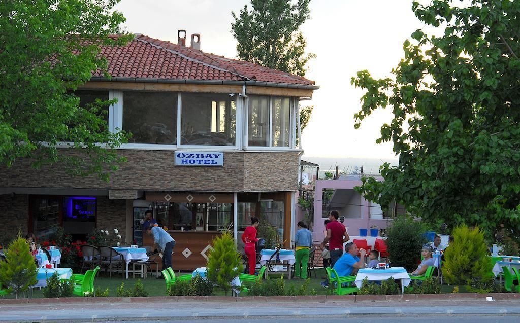 An outdoor seating area of a hotel with tables and chairs, a signboard, and a view of the surrounding greenery.