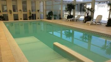 Una piscina interior con agua cristalina, rodeada de ventanas y plantas en macetas.