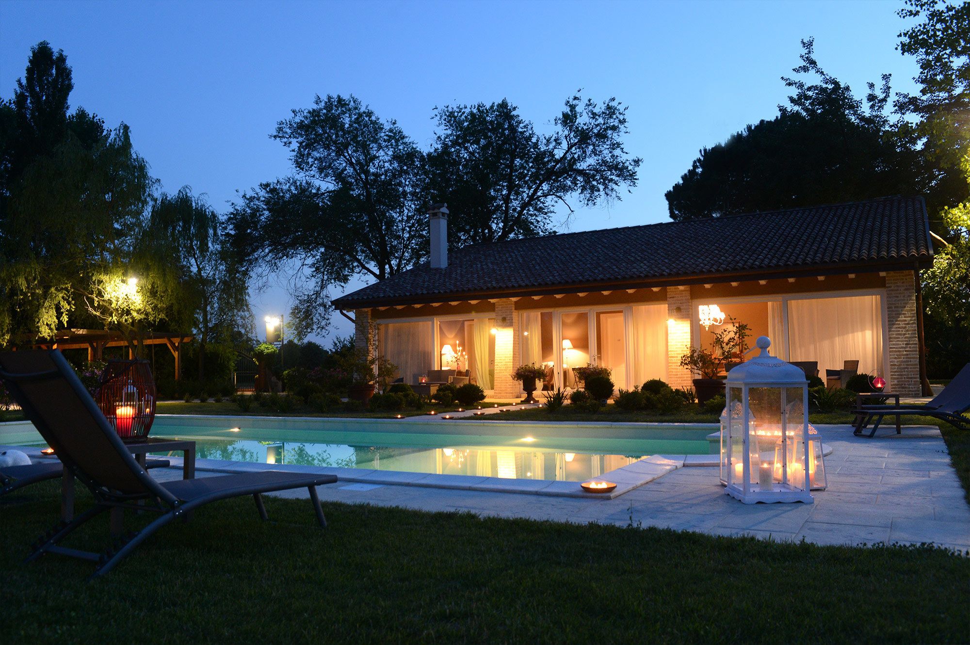 Une maison avec une piscine, un espace extérieur aménagé pour s’asseoir et une terrasse bien éclairée.