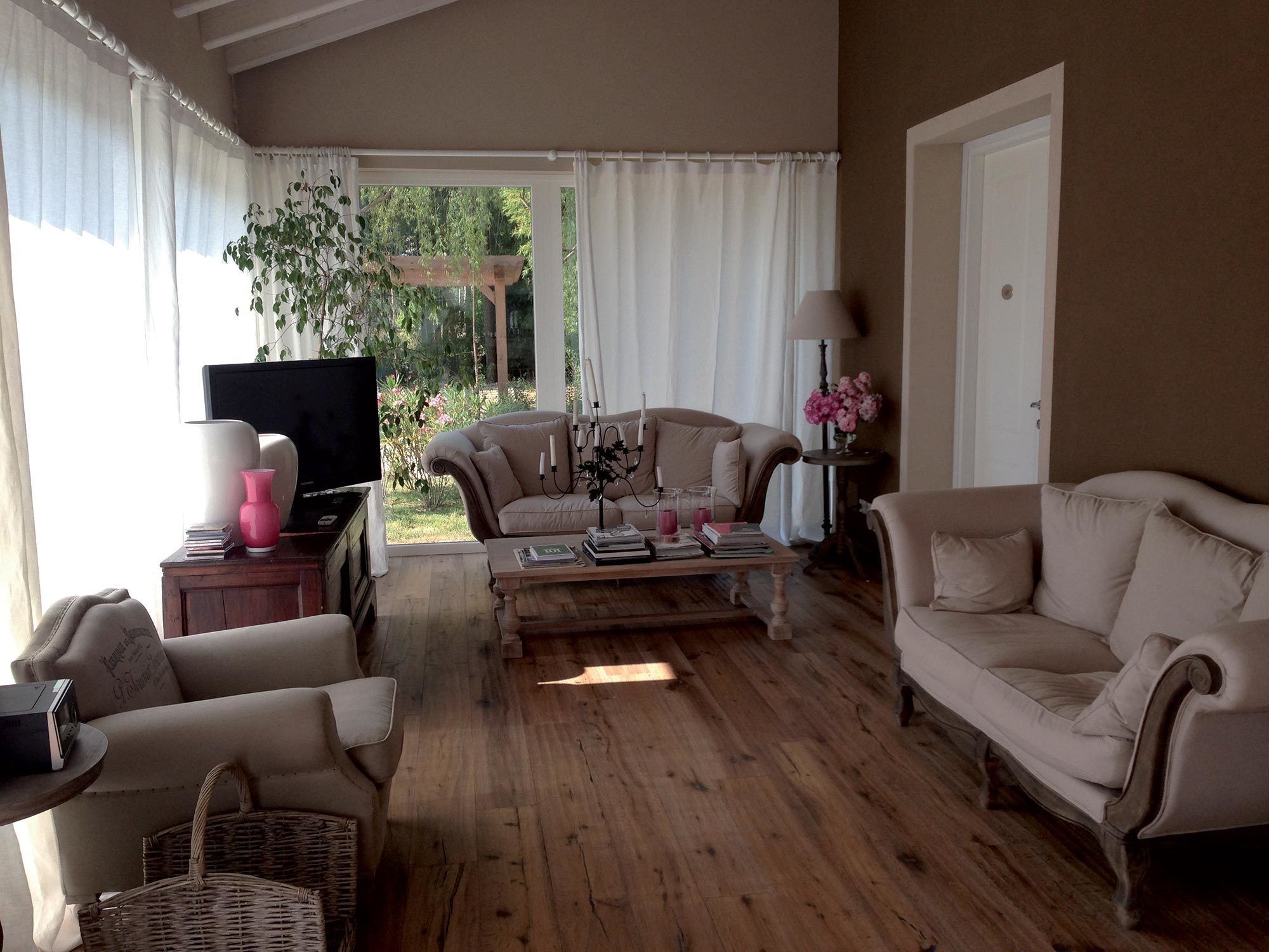 A cozy living room with a wooden floor, a beige sofa, a television, and a coffee table with books and drinks.