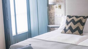Een keurig opgemaakt slaapkamer met een bed, een nachtkastje, een lamp en een bankje.