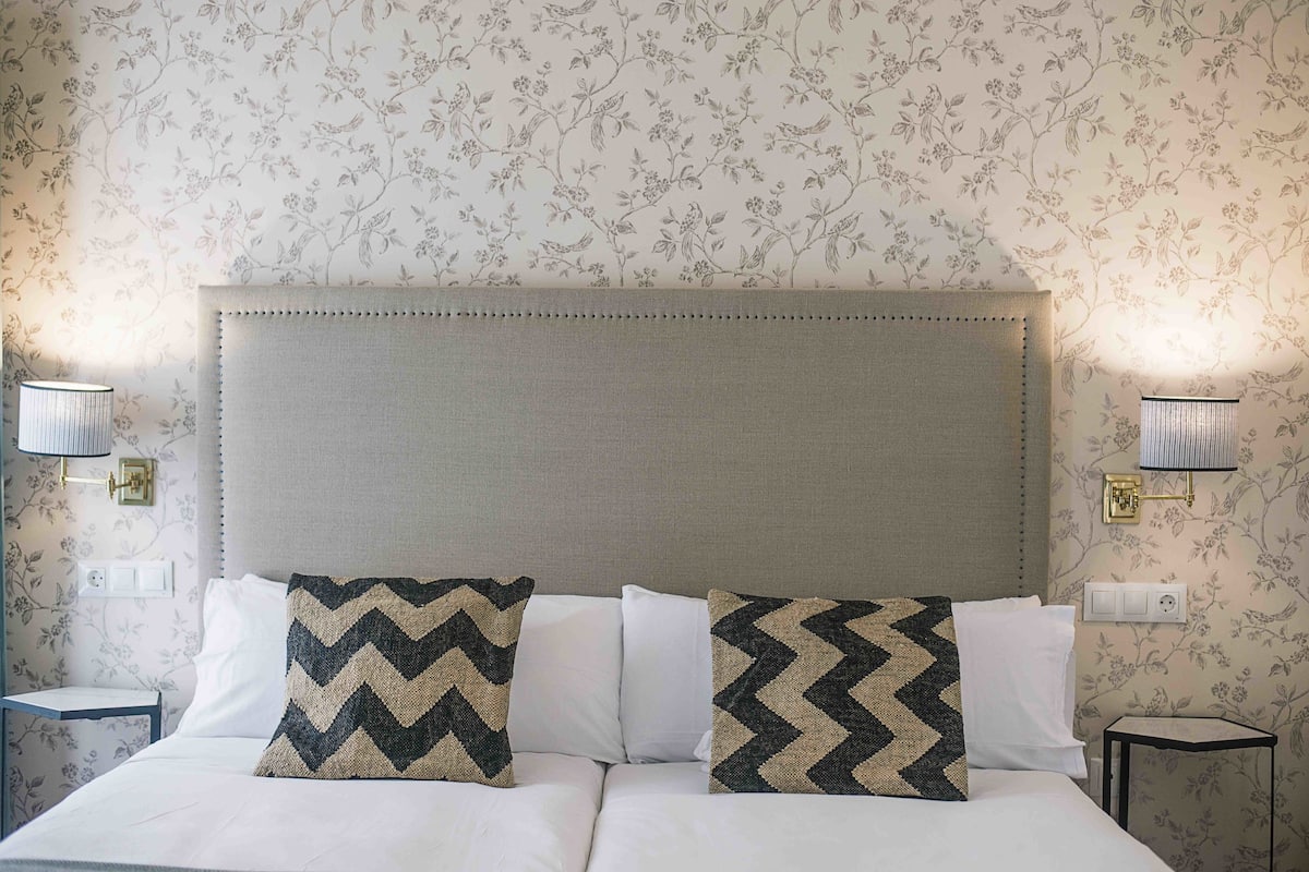 A hotel room with a large bed, two nightstands, and floral wallpaper.