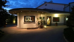 A modern house with a circular driveway, a well-lit entrance, and a small garden area. - Motel K (Casei Gerola)