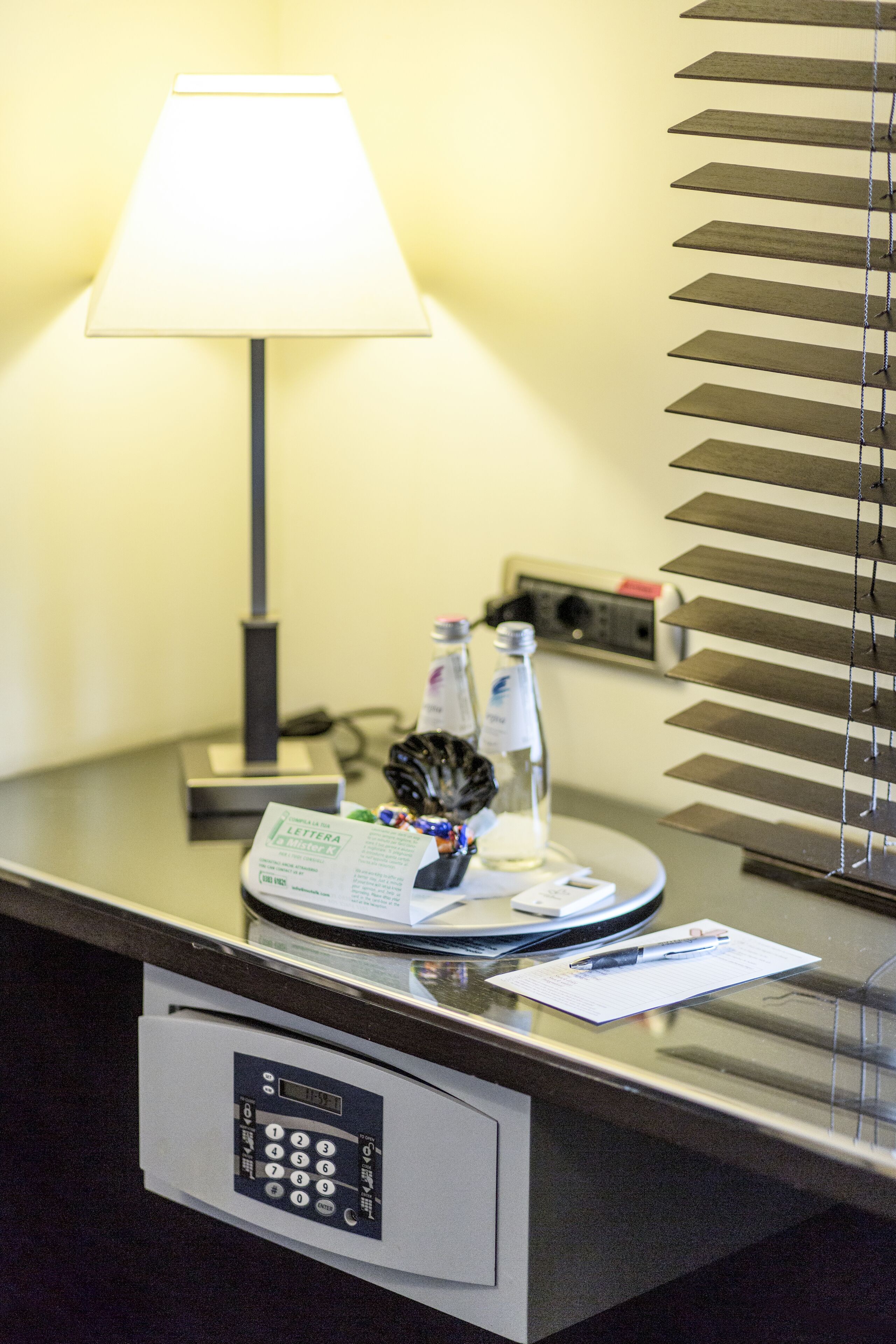 A hotel reception desk with a lamp, a telephone, a bottle, and a small decorative item.