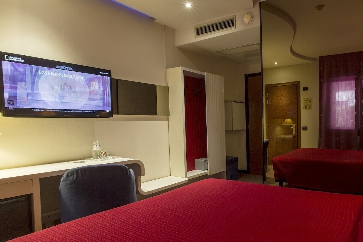 A hotel room with a bed, a desk, a television, and a door leading to another room.