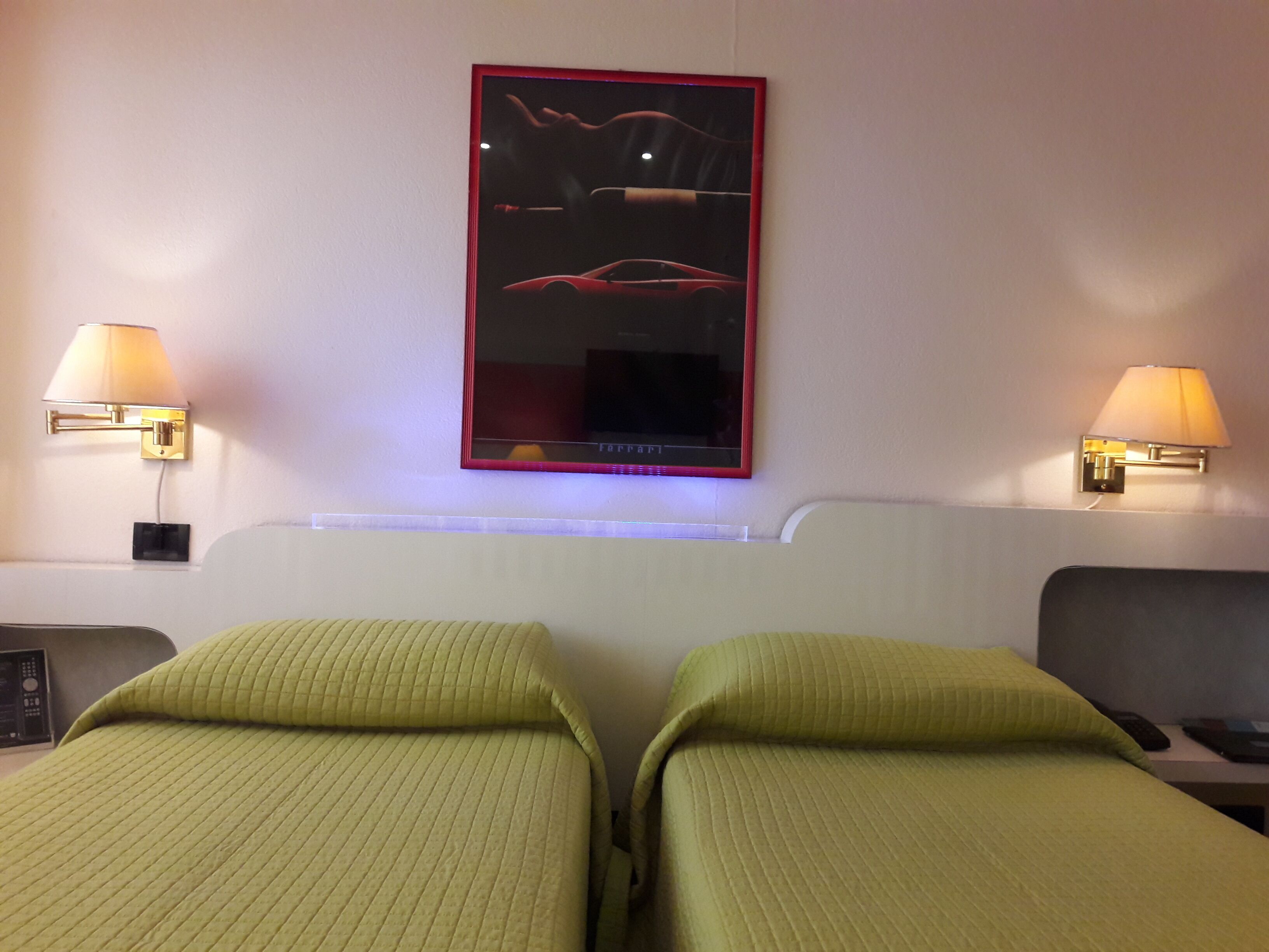 Une chambre d’hôtel avec deux lits simples, une table de chevet, une lampe et un tableau encadré au mur.
