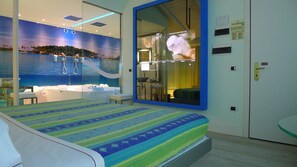 A hotel room with a bed, a large mirror, a bathroom with a bathtub, and a mural of a beach scene. - Motel K (Casei Gerola)