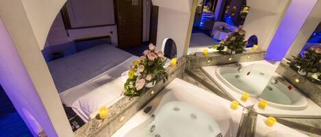 Un cuarto de spa con dos tinas separadas, una cama y un espejo que refleja la habitación.