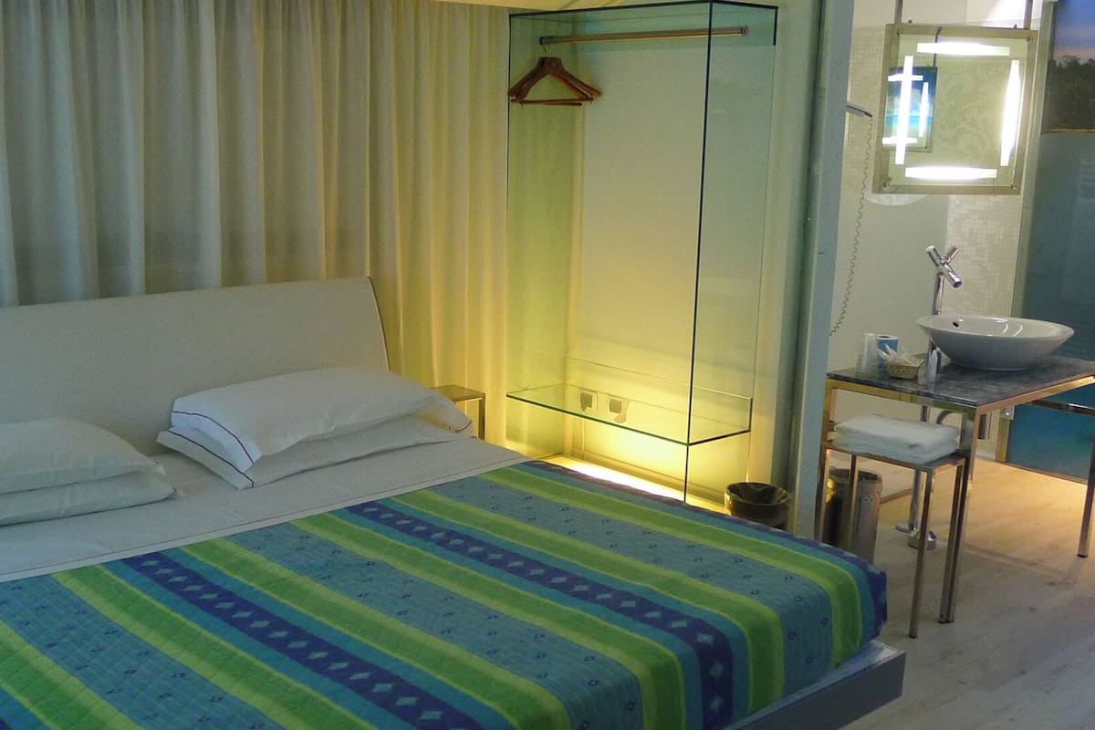 A hotel room with a bed, a bedside table, a mirror, and a bathroom with a sink.