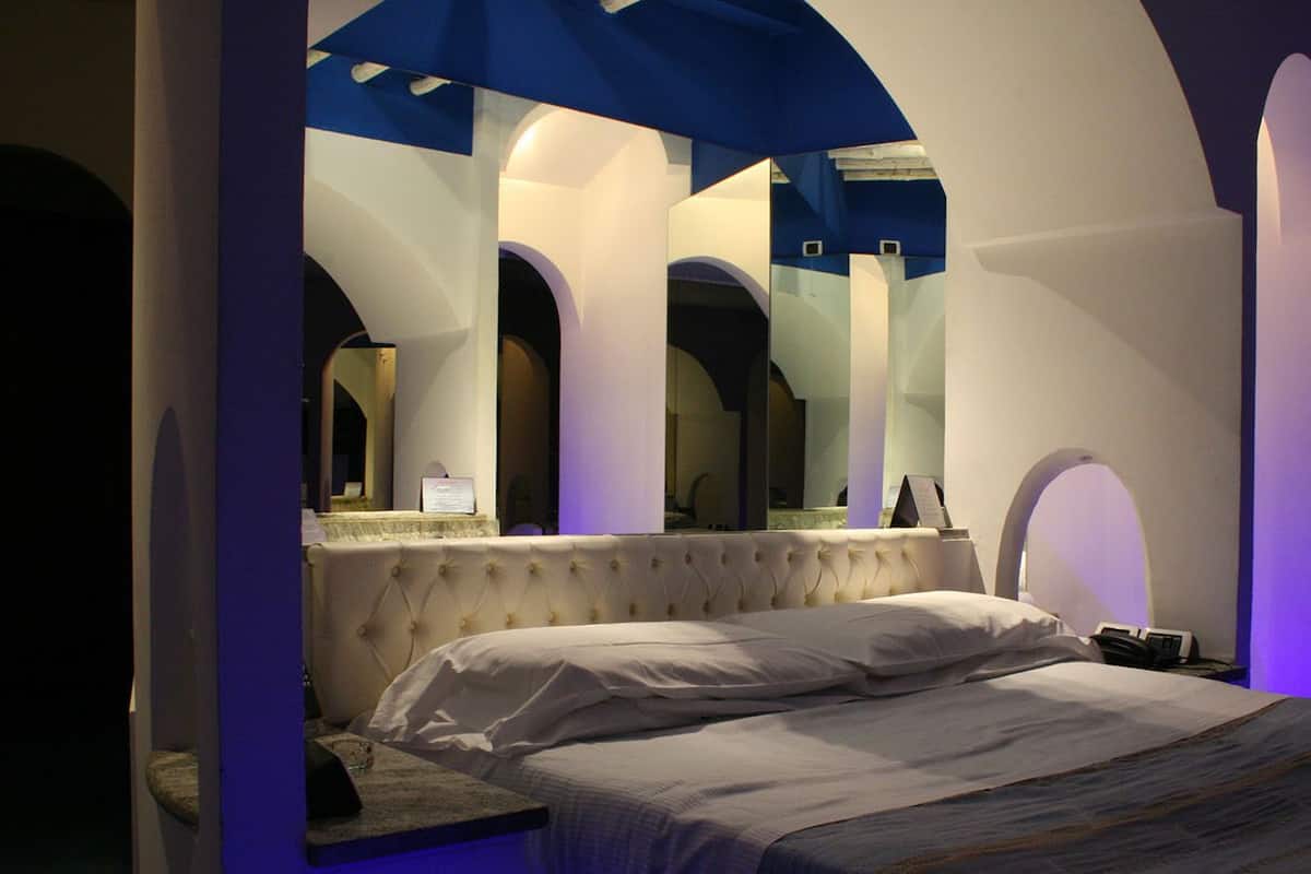 A bedroom with a large bed, a vanity with a mirror, and a unique arched ceiling design.