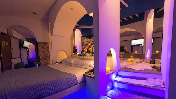 A modern hotel room with a bed, a sitting area with a chair, a small table, and a bathroom with a bathtub and towels. - Motel K (Casei Gerola)