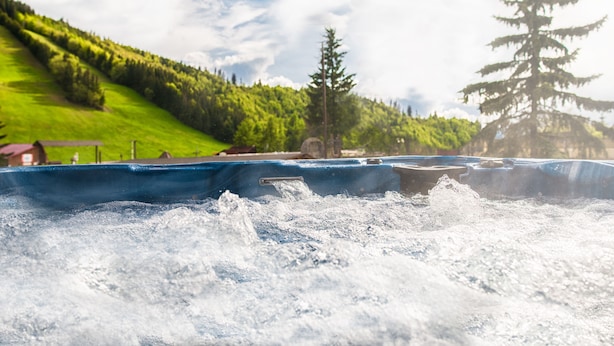 Un jacuzzi con vistas a una colina verde y un árbol.