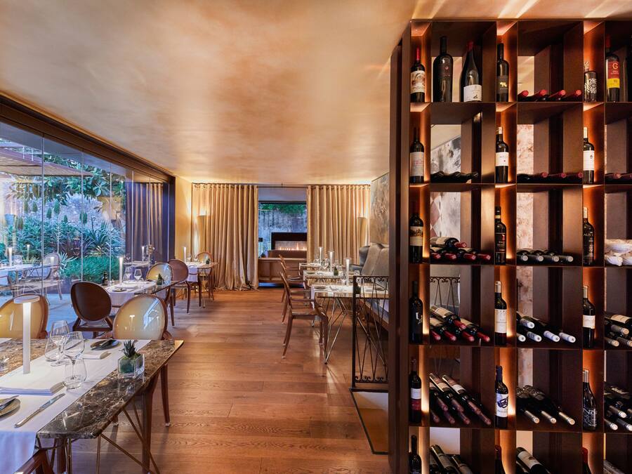 Un restaurante con una larga mesa de comedor, sillas y una estantería llena de botellas de vino.
