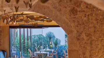 Un área de comedor al aire libre con mesas y sillas, rodeada de vegetación y un muro de piedra.