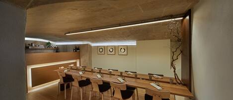 Un moderno comedor con una mesa de madera larga y sillas, una zona de cocina con mostrador, y una obra de arte colgada en la pared.