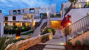 Un edificio moderno con una escalera que conduce a un segundo piso, rodeado de plantas en macetas y un muro de piedra.