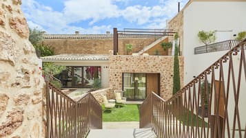 A courtyard with a stone wall, a wooden staircase, and a glass door leading to a room.