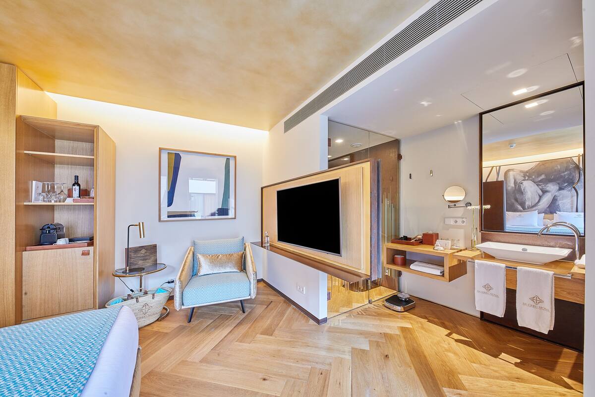 Une chambre d’hôtel moderne dotée d’un grand lit, d’un téléviseur à écran plat, d’une coiffeuse en bois avec un lavabo et d’un grand miroir.