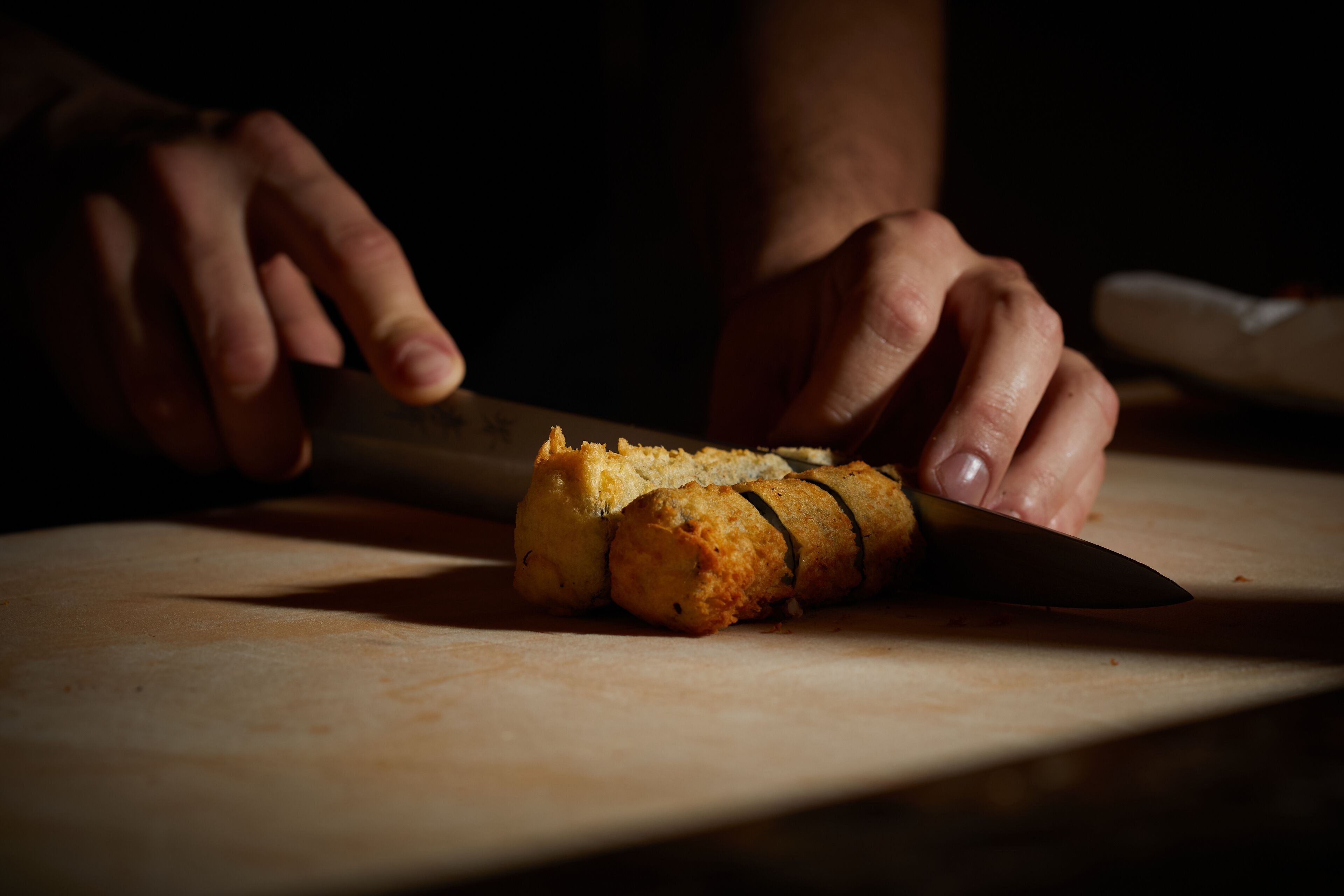 Manos cortando un trozo de comida sobre una tabla de cortar.