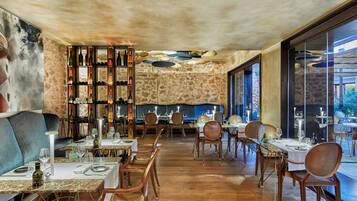 Ein Restaurantinnenraum mit Holztischen und -stühlen, Steinwänden und einem Weinkühlschrank.