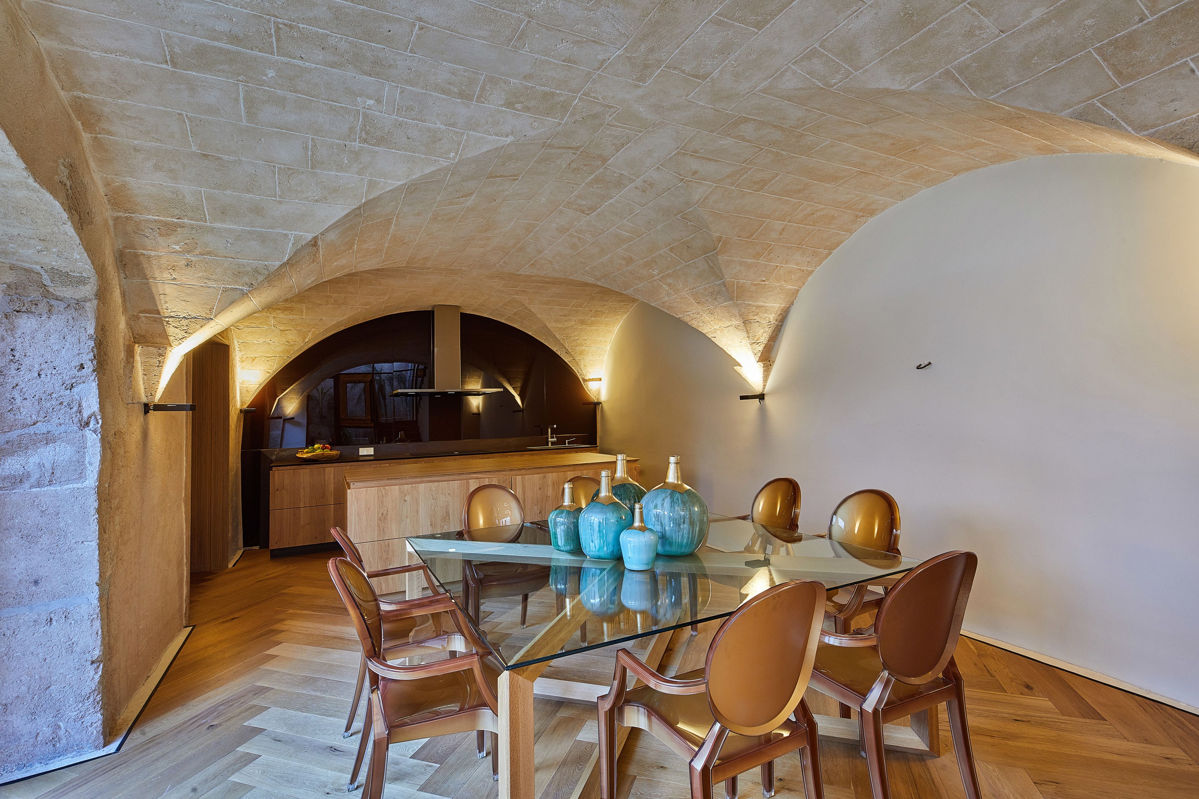 A dining area with a glass table, wooden chairs, and a kitchen in the background.