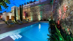 Una piscina con sillones de descanso, un muro de piedra y un edificio moderno al fondo.