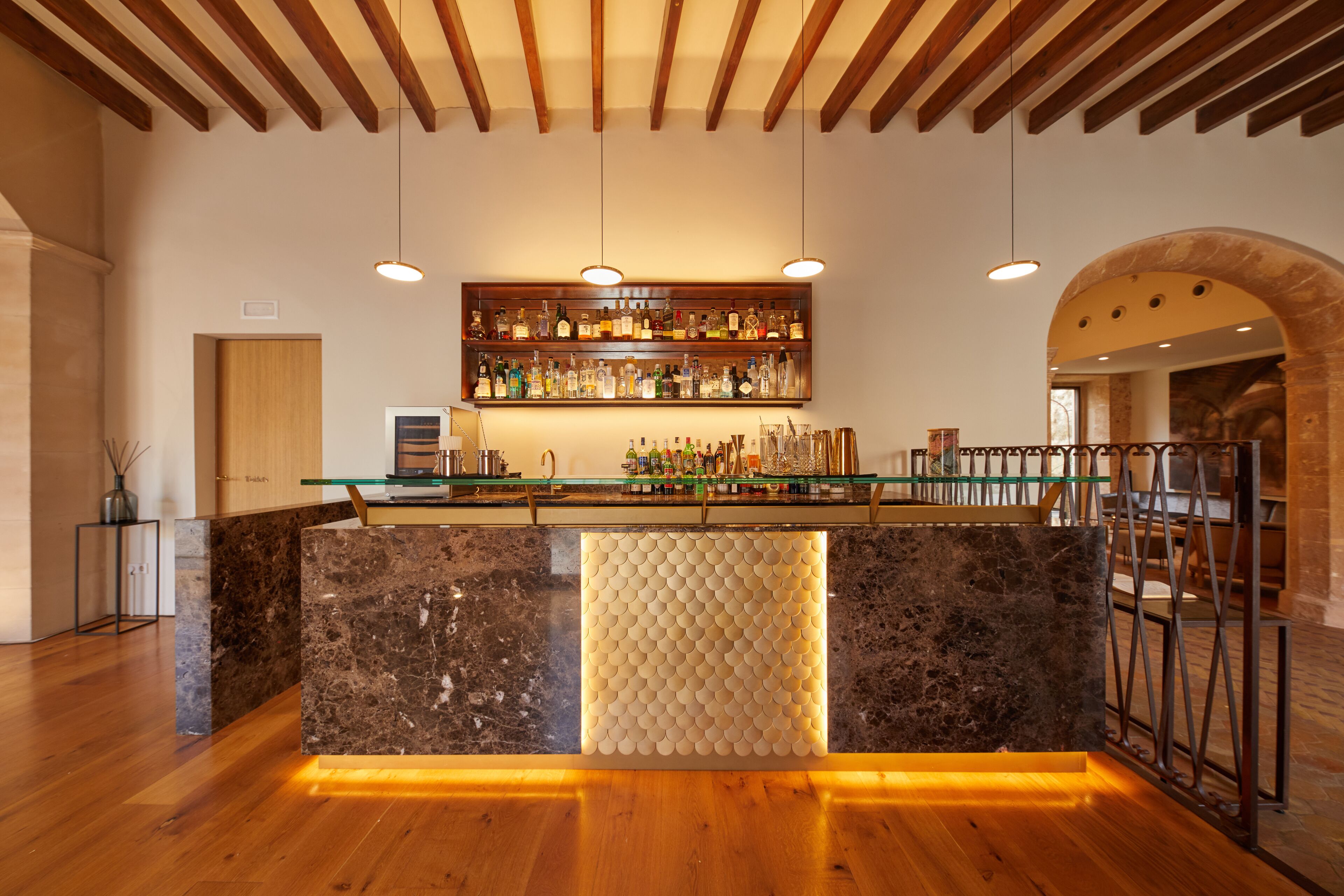 A bar area with a marble counter, wooden ceiling beams, hanging pendant lights, and a wine rack above.