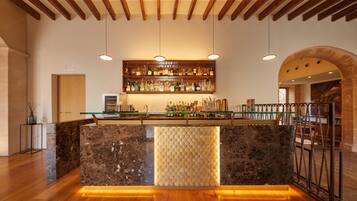 A bar area with a marble counter, wooden ceiling beams, hanging pendant lights, and a wine rack above.