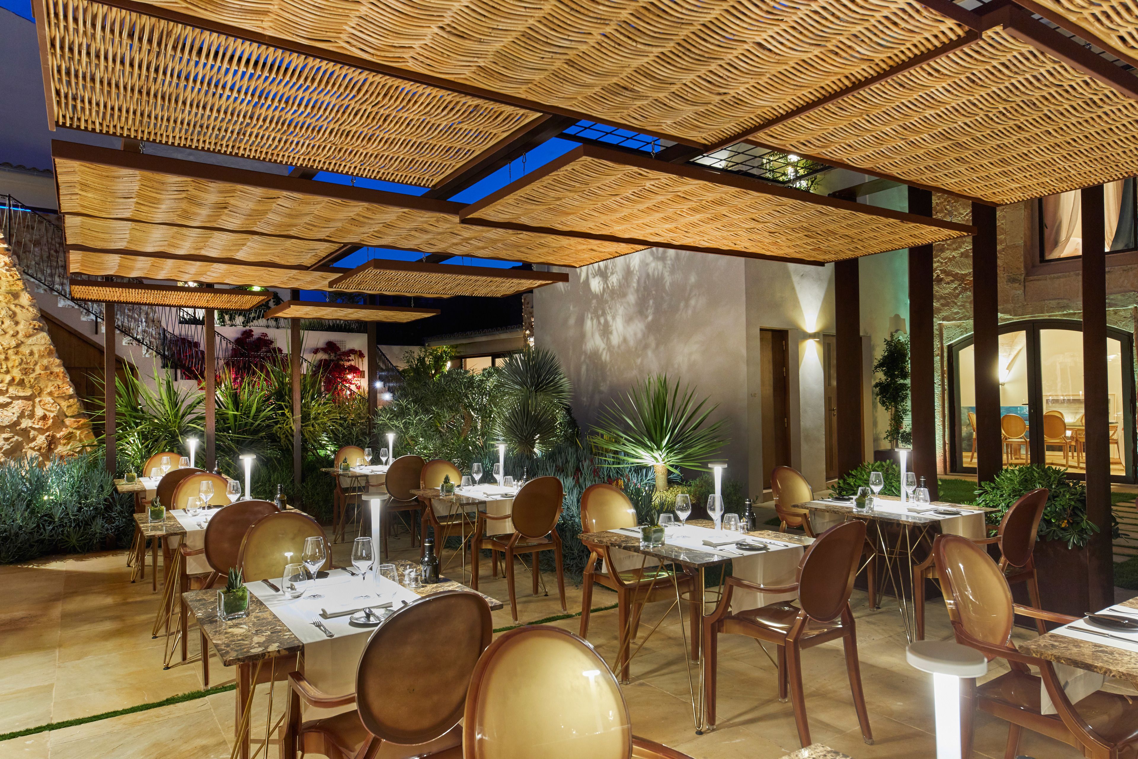 An outdoor dining area with tables and chairs, surrounded by plants and a stone wall.